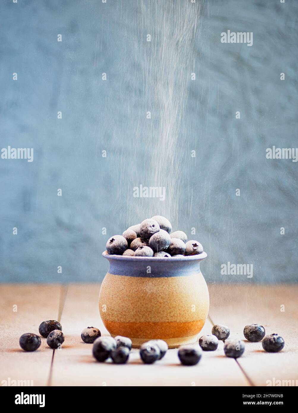 Une tasse en grès remplie de bleuets sur une surface en céramique.Poudre à épousseter tamisée sur les baies Banque D'Images