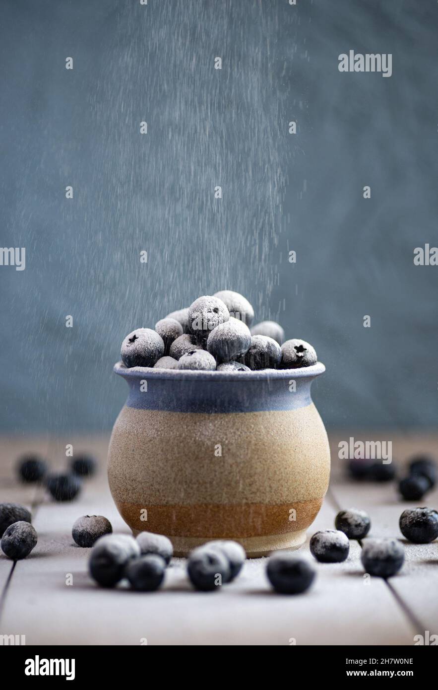 Une tasse en grès remplie de bleuets sur une surface en céramique.Poudre à épousseter tamisée sur les baies Banque D'Images