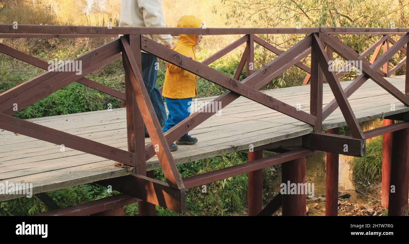 Maman avec un petit enfant marche sur un pont en bois au-dessus d'un ruisseau dans un parc d'automne Banque D'Images