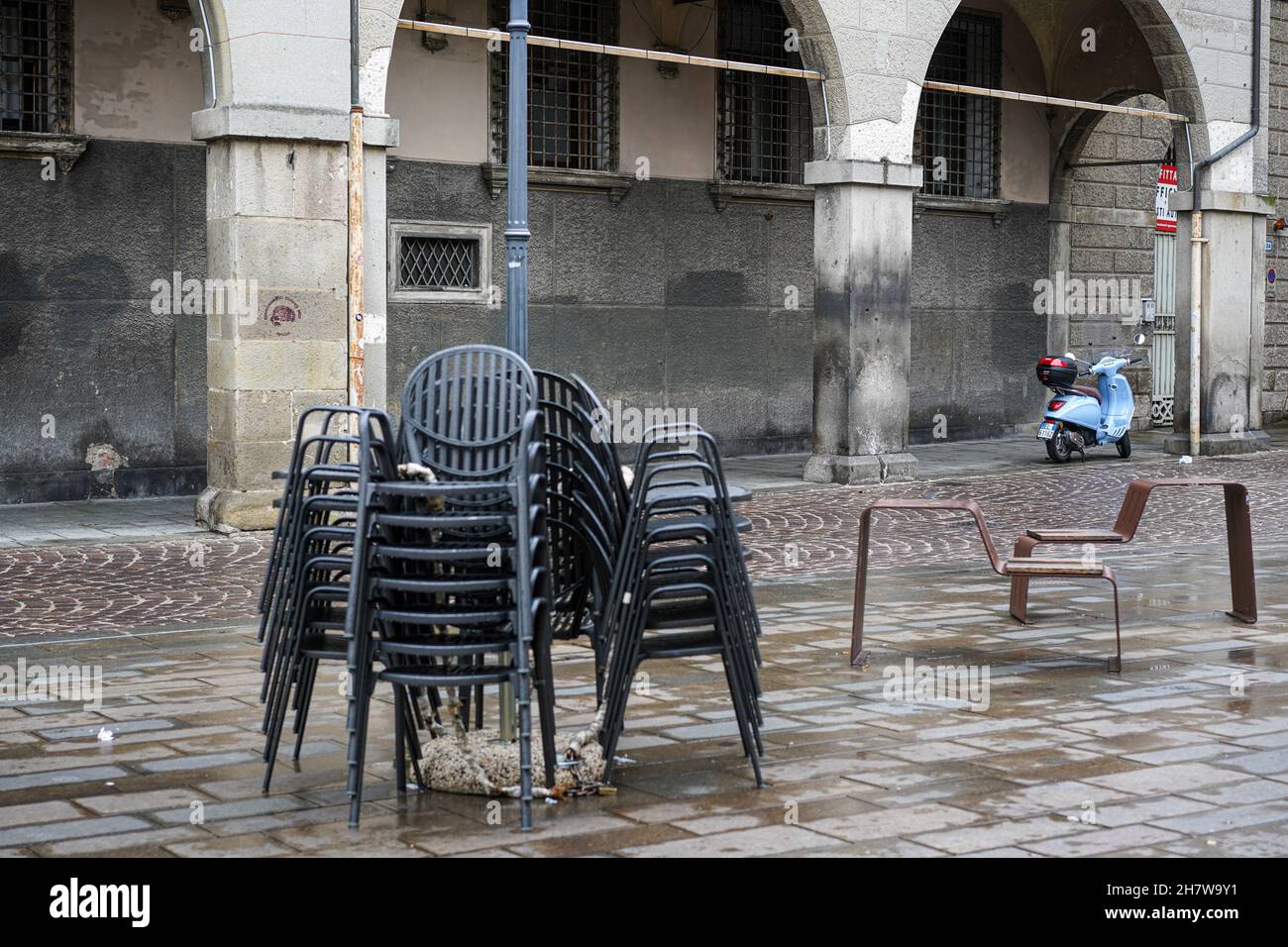 Des chaises noires empilées les unes sur les autres sur le trottoir pendant la pandémie de Corona en Italie. En arrière-plan, un Vespa bleu clair garé. Banque D'Images