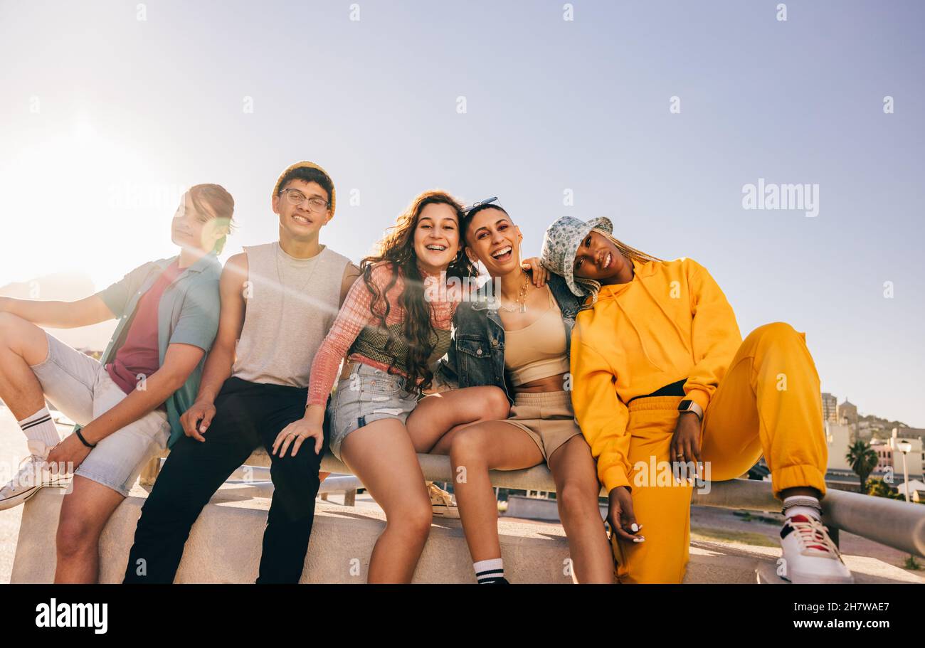 Divers groupes d'amis assis ensemble à l'extérieur au soleil.Les jeunes souriants sourient avec joie devant l'appareil photo.Génération z amis ayant un bon t Banque D'Images