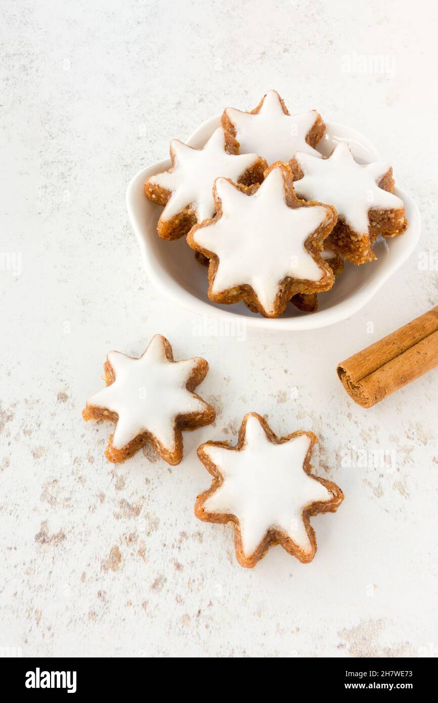 Biscuits aux étoiles de cannelle, Zimtsterne allemand traditionnel dans un bol blanc sur fond à motifs avec bâton de cannelle.Copier l'espace. Banque D'Images