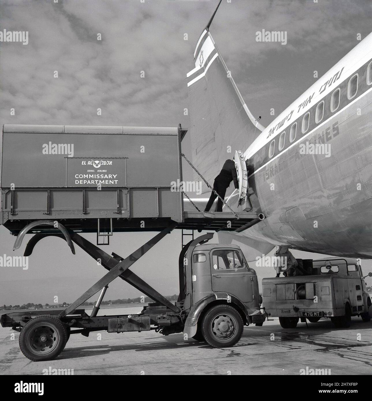 Années 1960, historique, à l'extérieur de l'aéroport de Londres, un avion El AL Boeing 707 stationné avec un conteneur du départ de l'agence Israel Airlines hissé à côté sur un camion de transport à grande hauteur, Londres, Angleterre, Royaume-Uni.Un agent de commissary se trouve sur la porte ouverte du conteneur pour charger des marchandises ou des allées à l'arrière de l'avion.Le travail de commissaire implique de se plier et de soulever régulièrement et d'être à l'extérieur par tous les temps. Banque D'Images