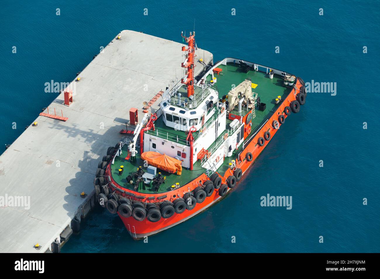 Bateau à remorqueurs avec coque rouge vif et pont vert est amarré près de quai en béton dans un port.Vue aérienne Banque D'Images