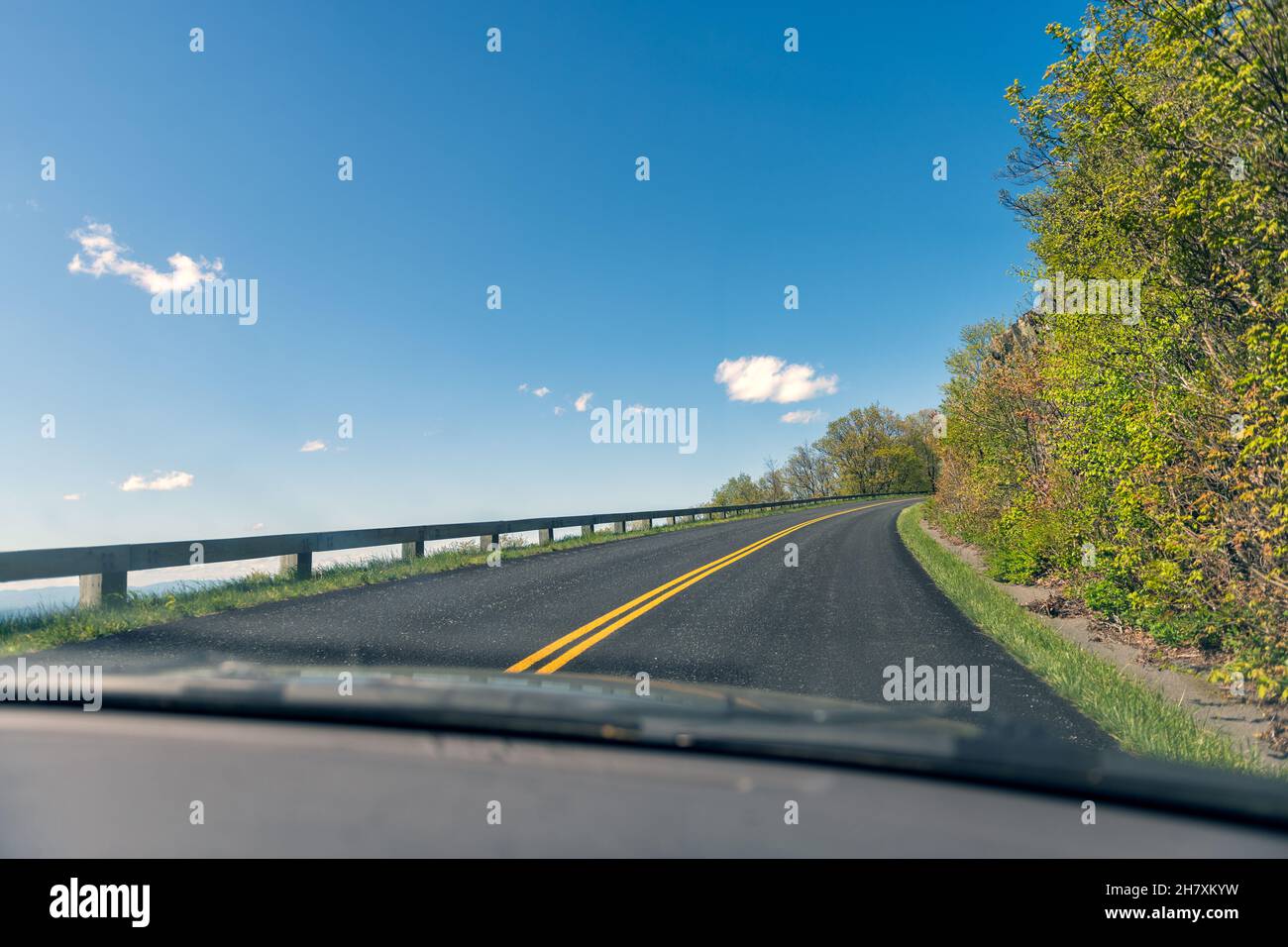 Point de vue de la voiture conduite sur la route sinueuse à travers le pare-brise dans Blue Ridge Mountains parkway en Virginie avec la route asphaltée pavée et le ciel bleu Banque D'Images