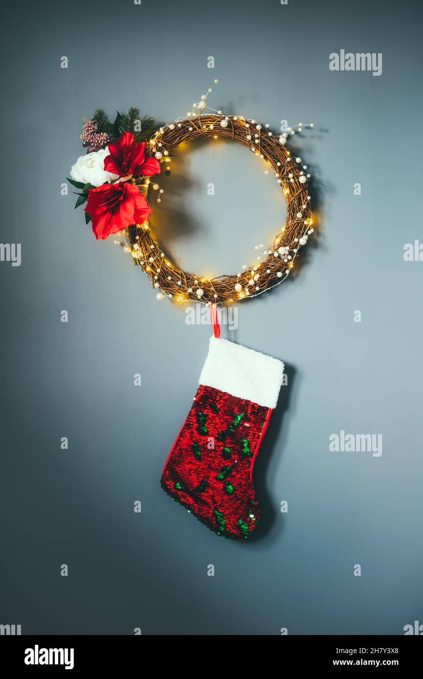 Couronne de fleurs moderne faite de branches tissées, perles et lumières avec des sequins rouges suspendus bas de Noël sur le mur gris.Décoration de fête minimaliste Banque D'Images