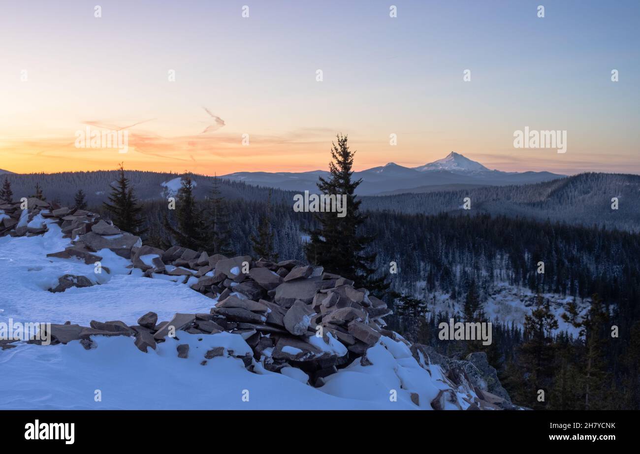 Vue sur les sommets enneigés pendant un coucher de soleil orange, dans les rochers montagneux en premier plan dans la neige, Mt.Hood National Forest, Oregon, États-Unis Banque D'Images
