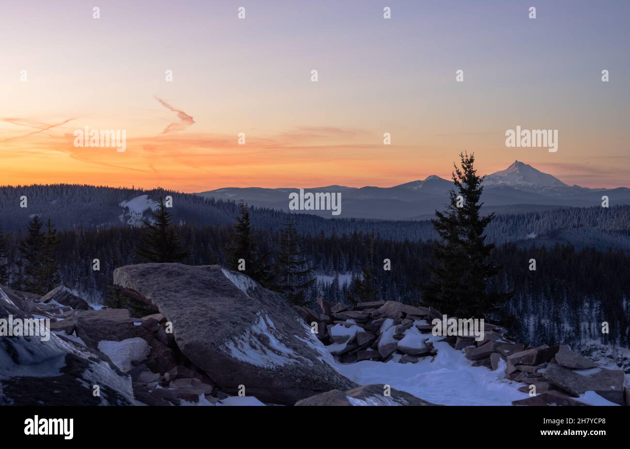 Vue sur les sommets enneigés pendant un coucher de soleil orange, dans les rochers montagneux en premier plan dans la neige, Mt.Hood National Forest, Oregon, États-Unis Banque D'Images