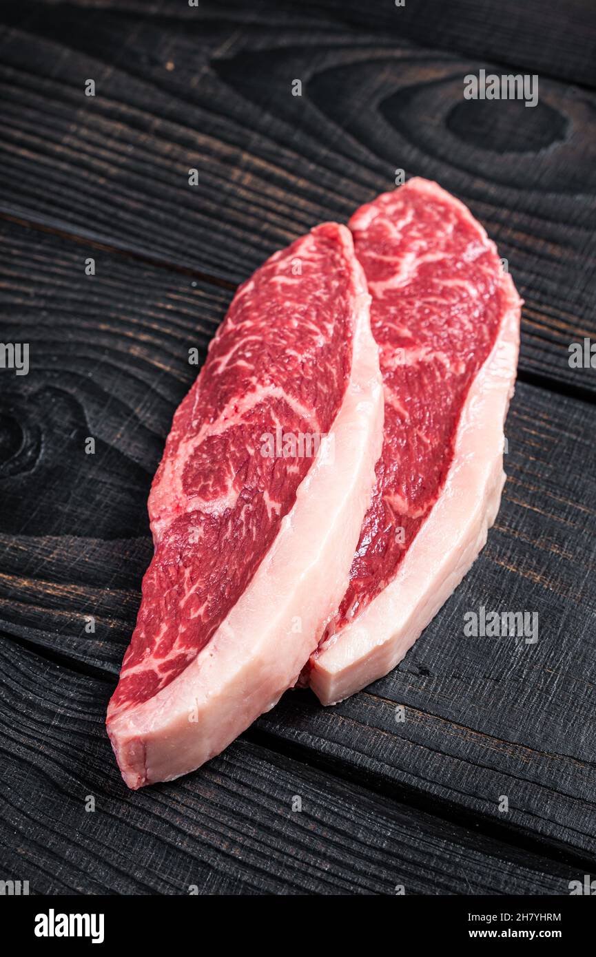 Steak de bœuf cru ou bifteck de viande de bœuf au chapeau de sirloin sur la table de boucher. Arrière-plan en bois noir. Vue de dessus Banque D'Images