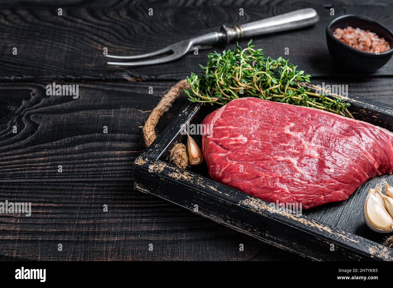 Steak de viande de bœuf coupé au sommet de la sirloine crue ou Picanha dans un plateau en bois avec des herbes. Arrière-plan en bois noir. Vue de dessus. Copier l'espace Banque D'Images