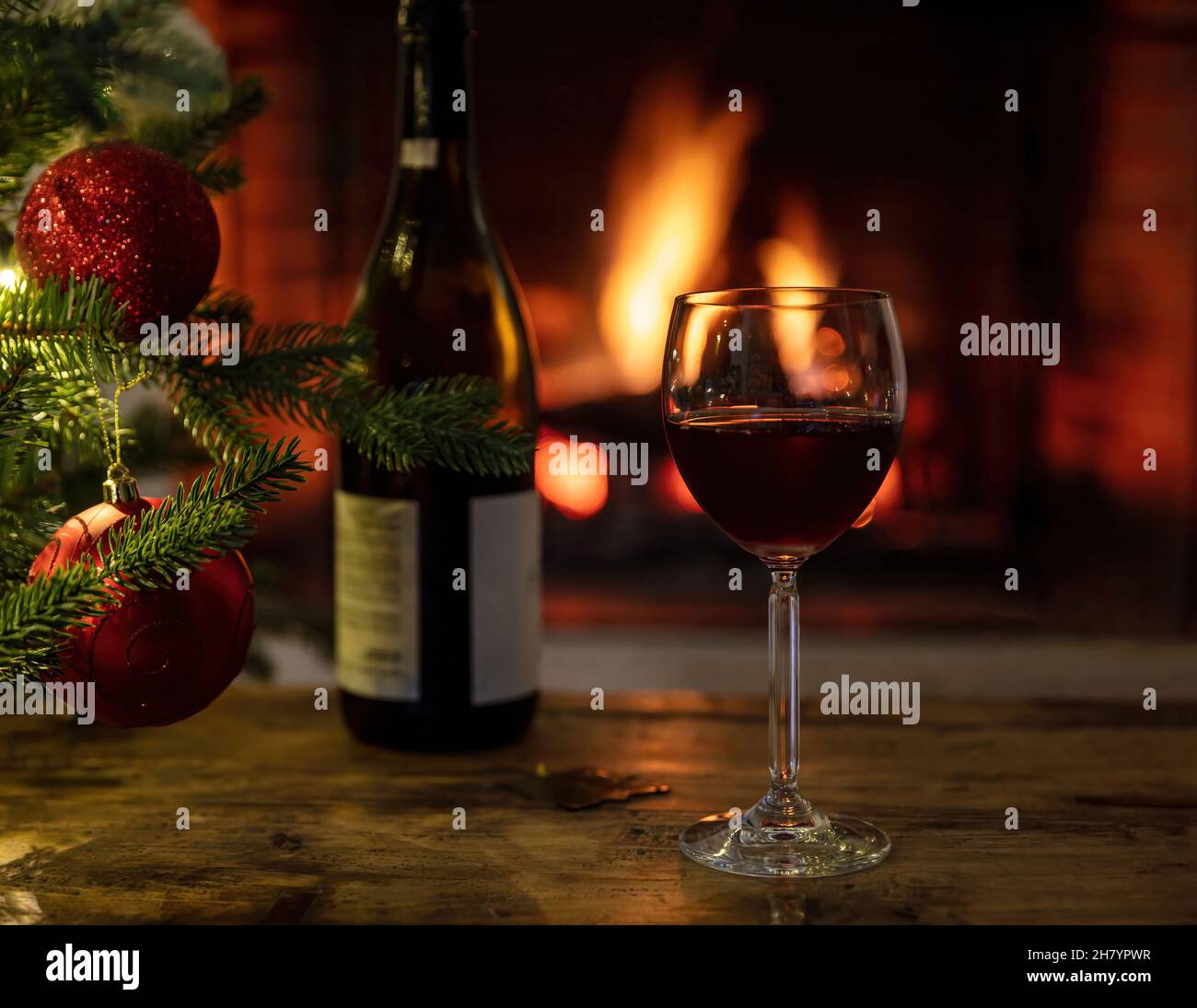 Noël, verre de vin rouge et bouteille sur une table en bois, foyer en arrière-plan.Décoration arbre de Noël.Confortable maison chaude, vacances d'hiver détente Banque D'Images