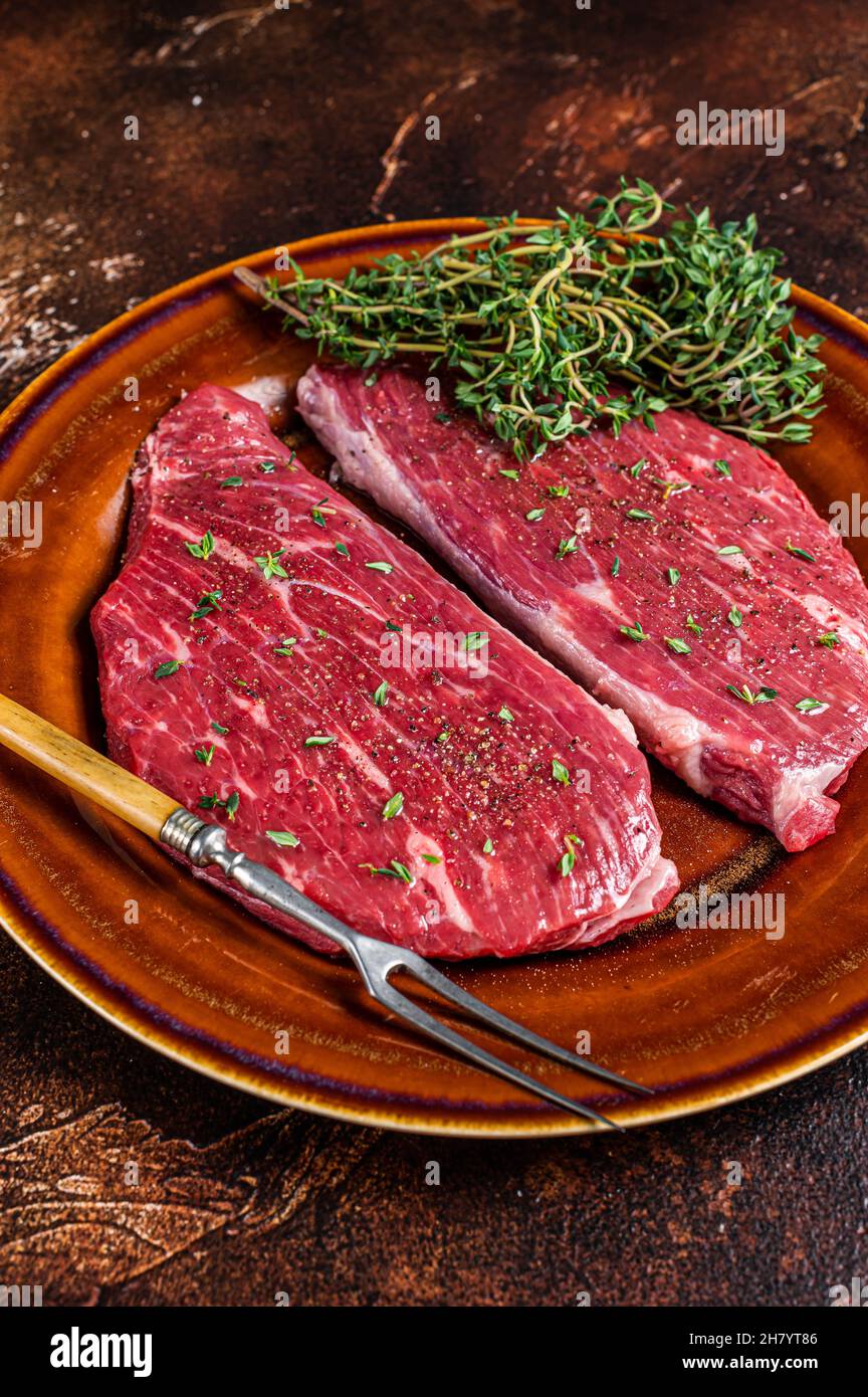 Steak de calotte cru ou steak d'aloyau dans une assiette rustique au thym et à l'huile d'olive. Arrière-plan sombre. Vue de dessus Banque D'Images