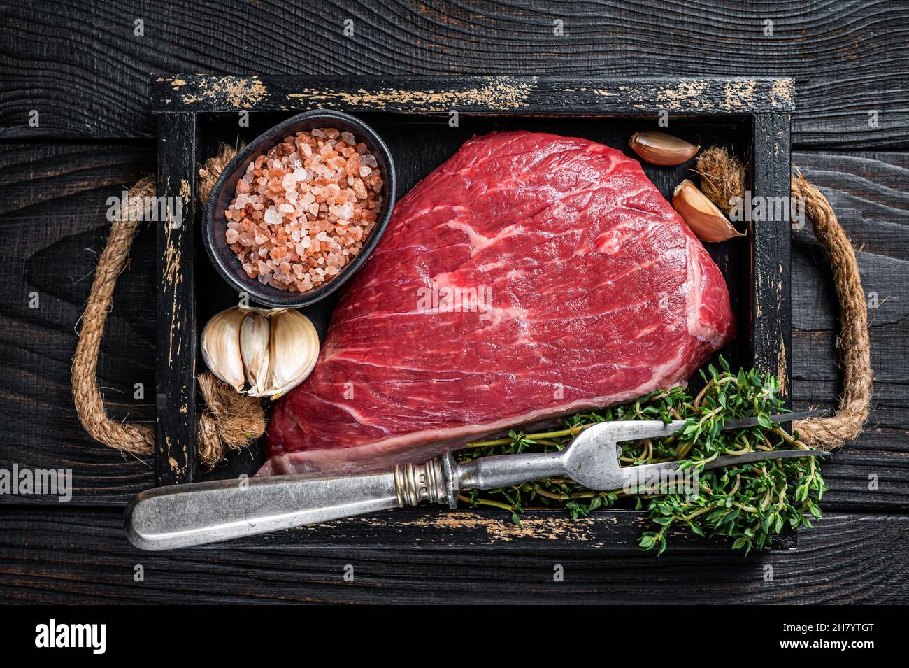Steak de viande de bœuf coupé au sommet de la sirloine crue ou Picanha dans un plateau en bois avec des herbes. Arrière-plan en bois noir. Vue de dessus Banque D'Images