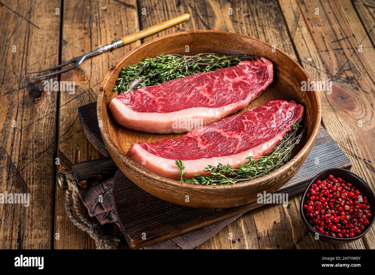 Steaks de viande de boeuf non cuits en haut cru au sommet de sirloin dans une assiette en bois avec des herbes. fond de woden. Vue de dessus Banque D'Images
