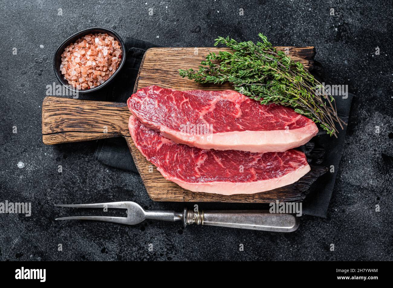 Steak de rumsteck cru non cuit ou biftecks de viande de bœuf au chapeau de sirloin sur une planche de bois. Arrière-plan noir. Vue de dessus Banque D'Images