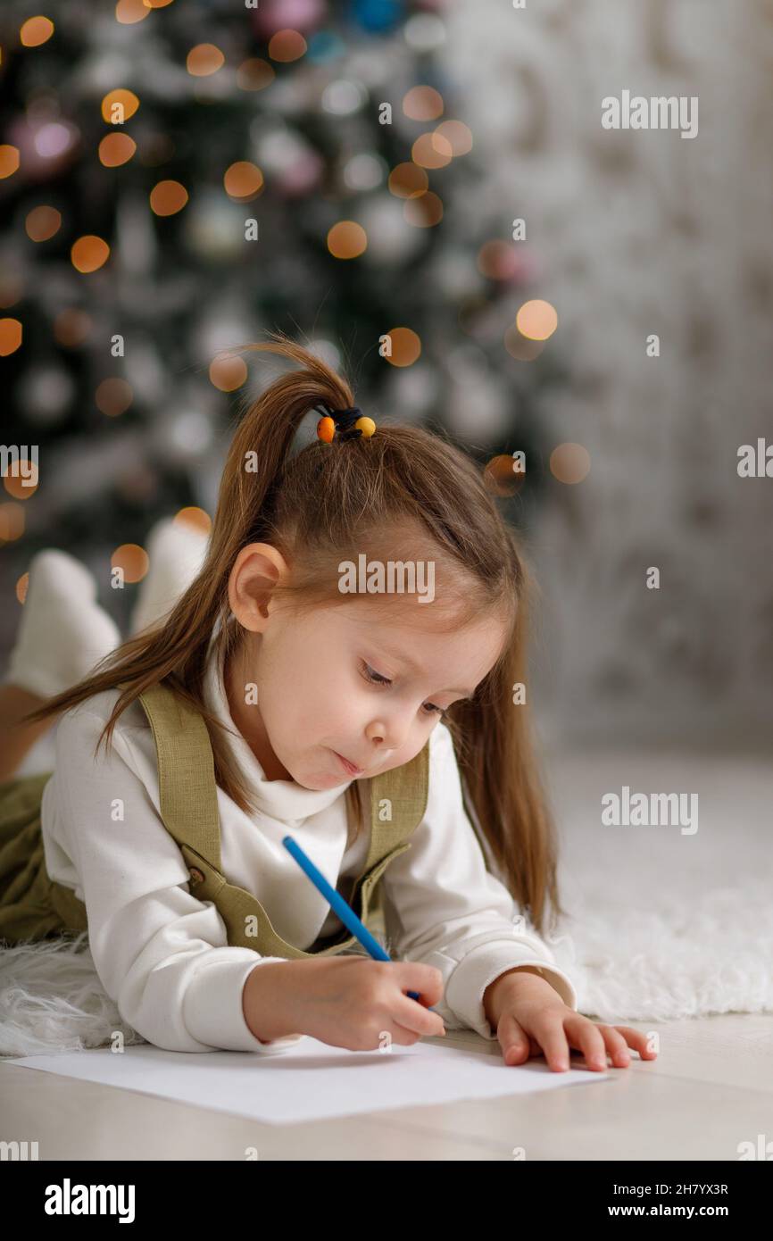 Une petite fille mignonne avec des queues de cheval écrit une lettre au père noël, un espace de copie vertical. Banque D'Images