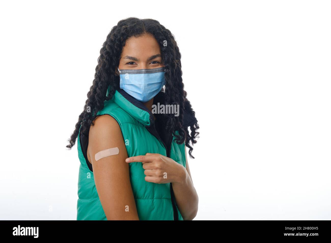 Une femme latine portant un masque facial tout en montrant son bras avec un aide-bande après avoir reçu le vaccin contre le covid-19. Banque D'Images