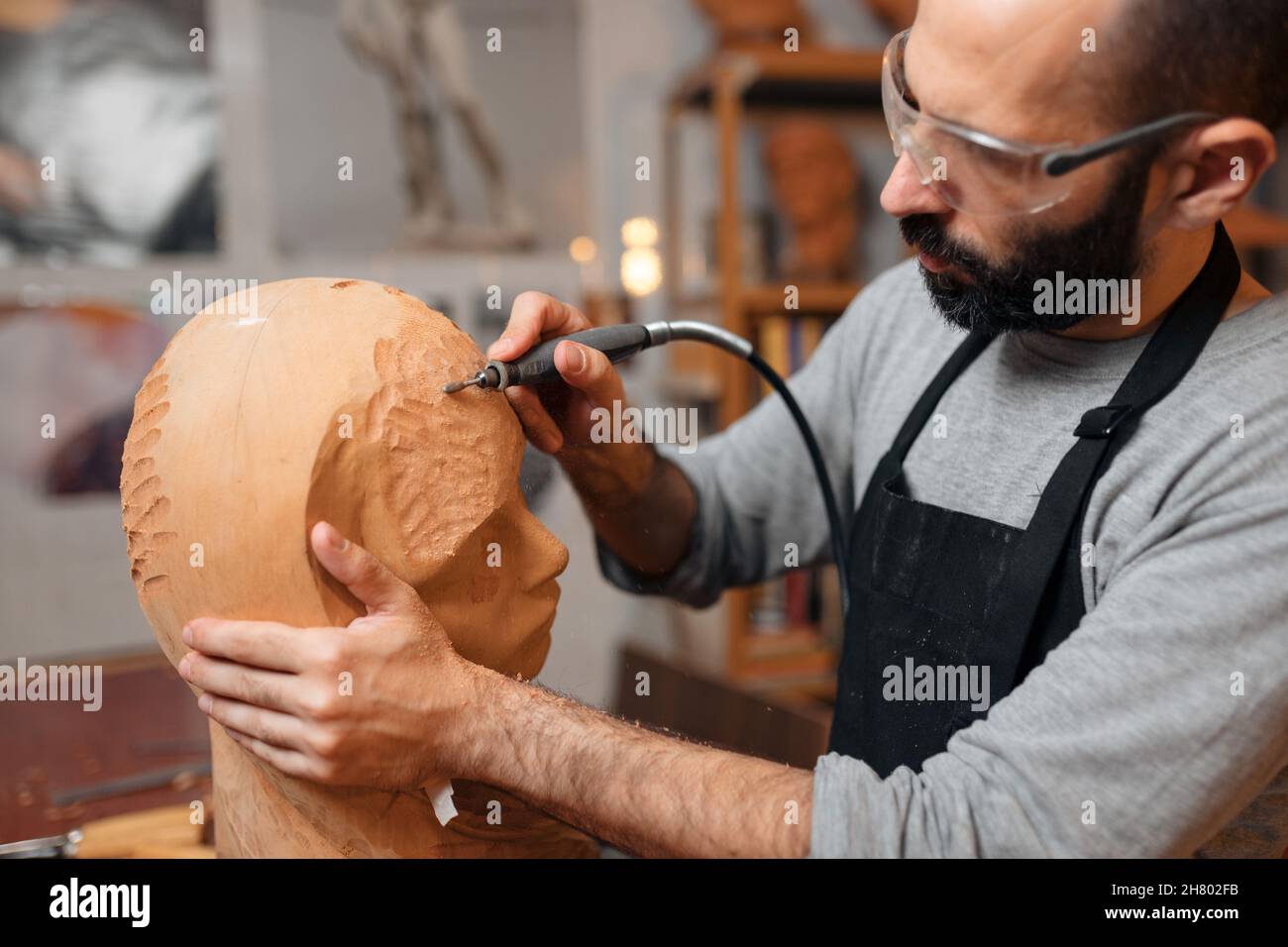 Menuiserie masculine en tablier et lunettes de protection sculptant une sculpture en bois avec un outil de gravure professionnel tout en travaillant dans la menuiserie légère Banque D'Images