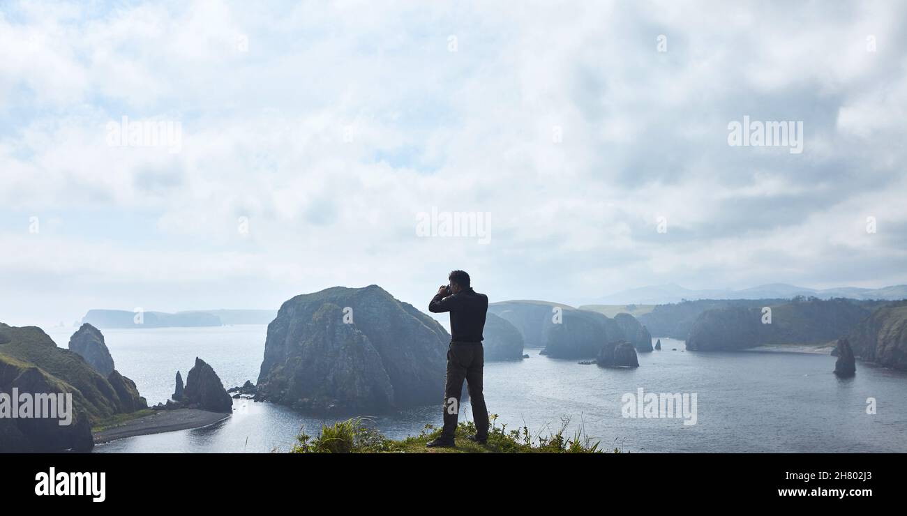 Un photographe masculin prend des photos sur fond d'une magnifique baie.Le rétroéclairage et un grand espace de ciel et de baie créent une atmosphère inhabituelle Banque D'Images