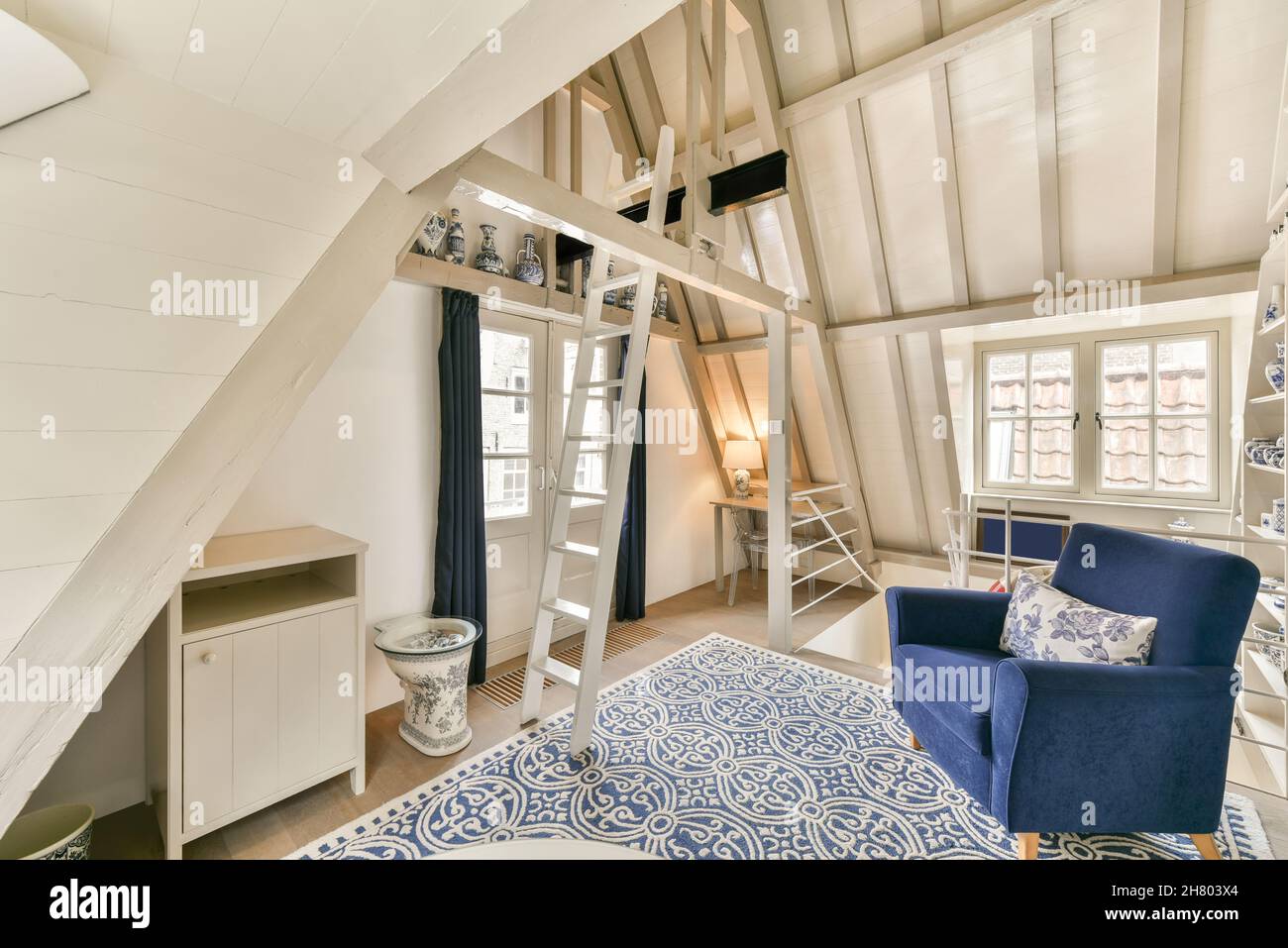Fauteuil bleu avec oreiller placé sur la moquette près de l'échelle blanche dans le grenier clair avec des fenêtres et vases en céramique dans l'appartement Banque D'Images