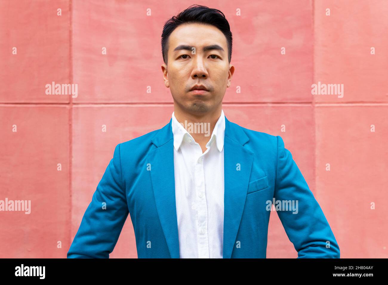 Homme asiatique plein de confiance en tenue habillée dans une élégante  veste de costume bleue regardant l'appareil photo tout en étant debout dans  la rue près d'un mur lumineux en ville Photo