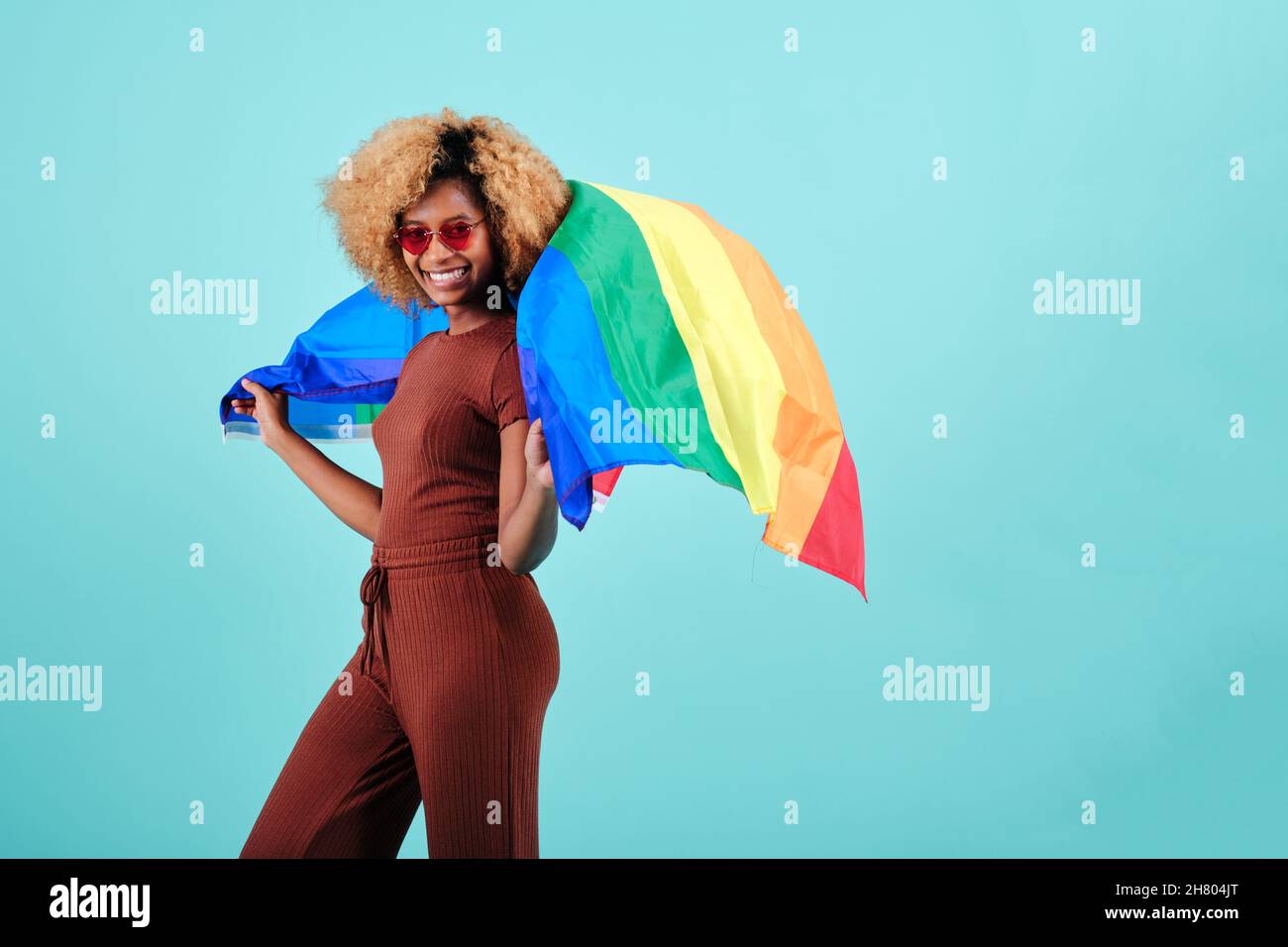 Jeune femme afro joyeuse agitant un drapeau de fierté sur un fond isolé. Banque D'Images