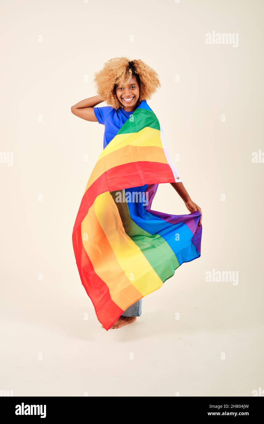 Femme souriante aux cheveux bouclés portant un drapeau arc-en-ciel de fierté lgbt sur un fond isolé. Banque D'Images