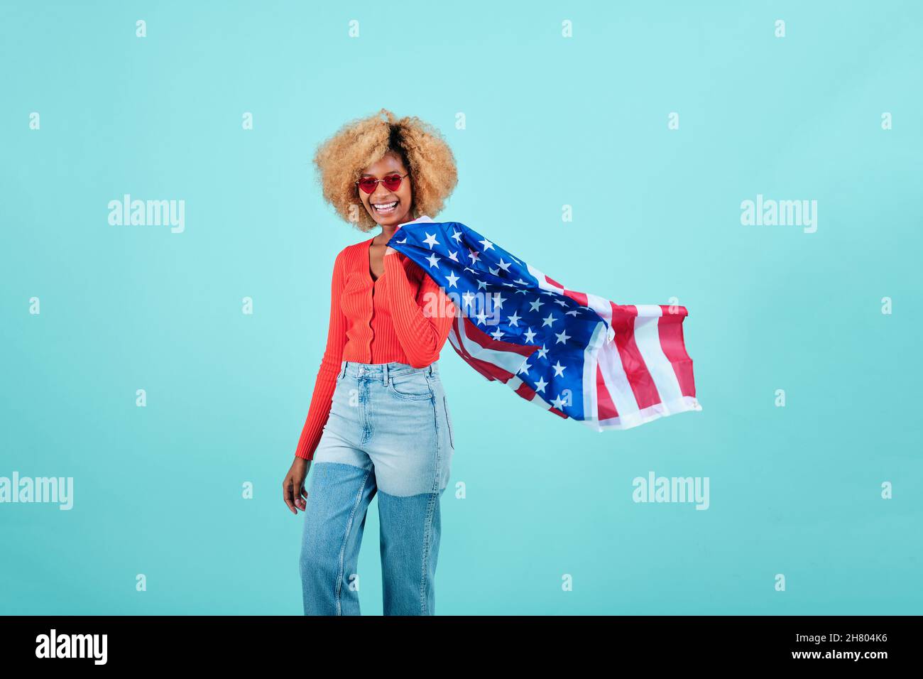 Jeune femme souriant tout en tenant un drapeau américain sur un fond isolé. Banque D'Images