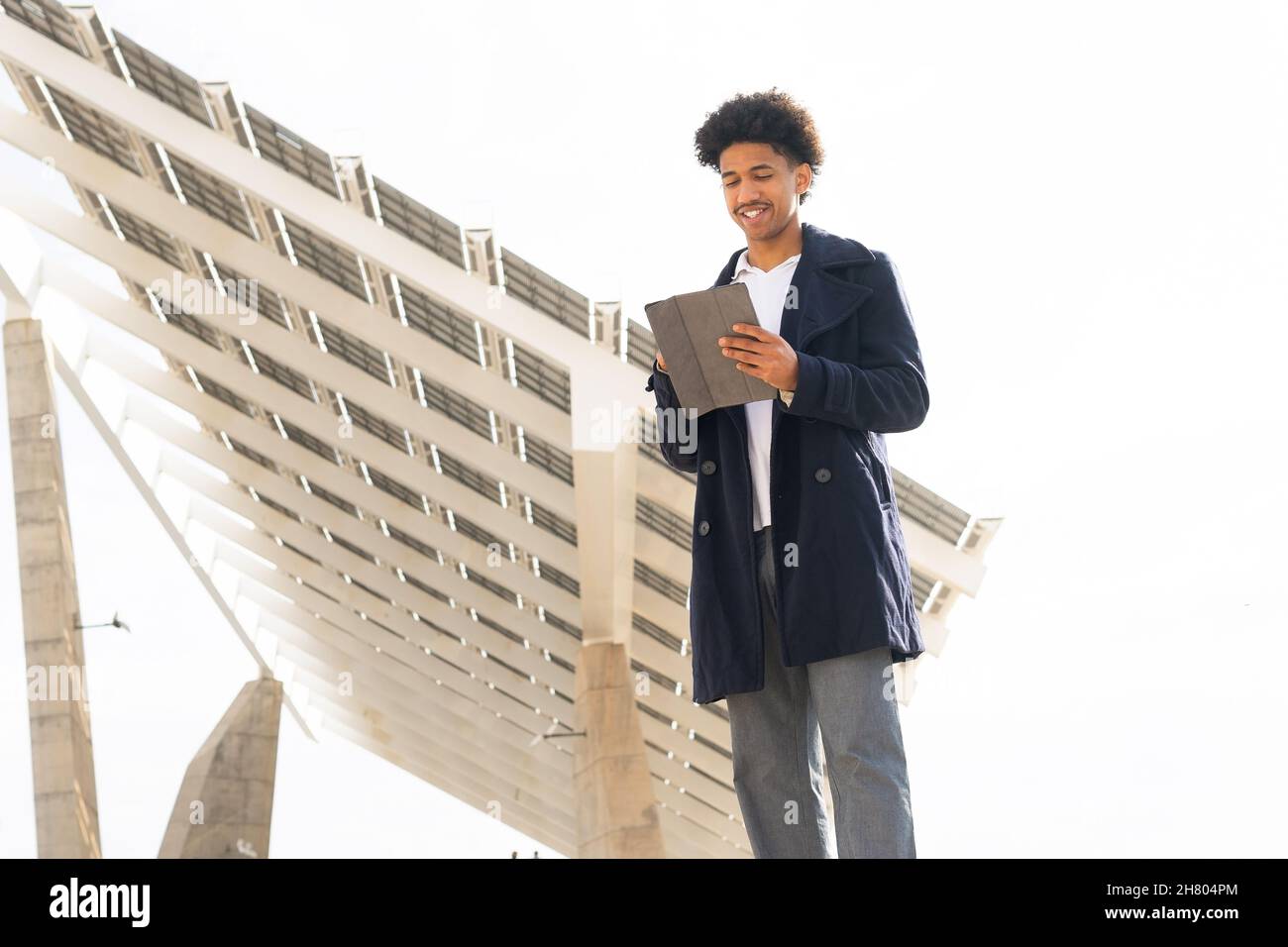 Faible angle de positif Afro-américain mâle avec des boucles Afro portant des vêtements d'extérieur souriant largement tout en défilant tablette à l'extérieur Banque D'Images