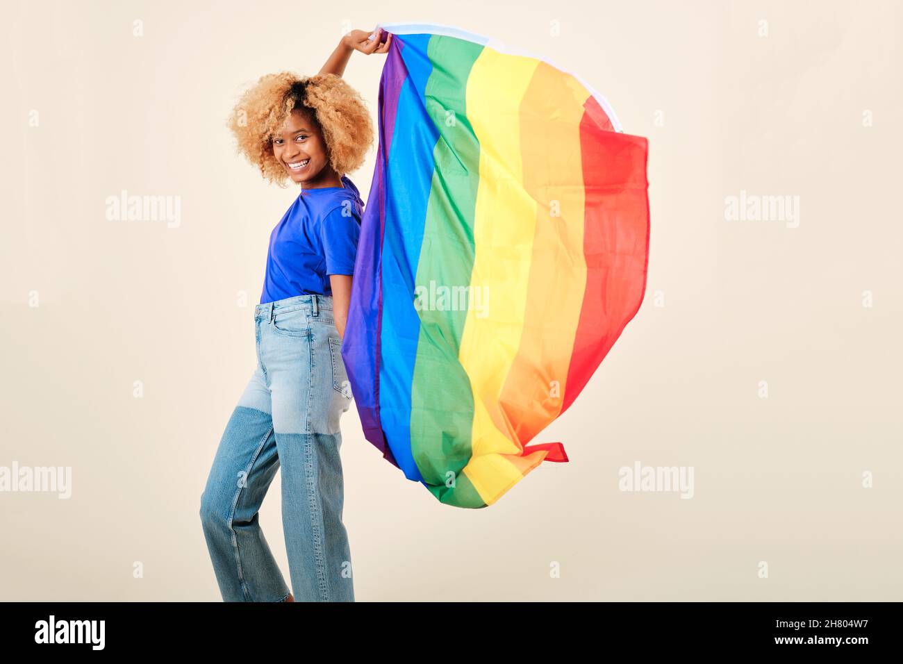 Femme afro souriant tout en tenant le drapeau lgbtq de la fierté gay sur un fond isolé. Banque D'Images