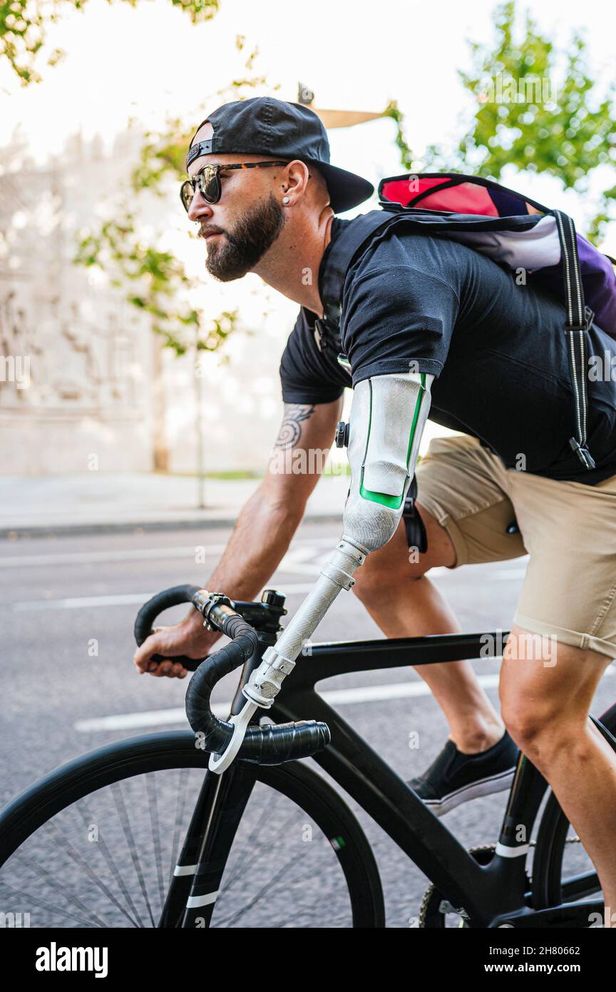 Vue latérale de l'hipster mâle barbu avec bras artificiel à vélo le long de la rue en été dans la ville Banque D'Images