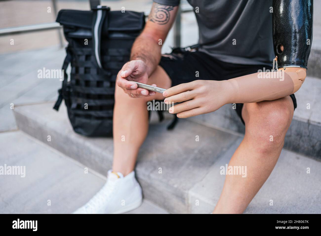 Grand angle de récolte anonyme mâle avec bras en caoutchouc artificiel de navigation téléphone mobile tout en étant assis sur les escaliers dans la ville Banque D'Images