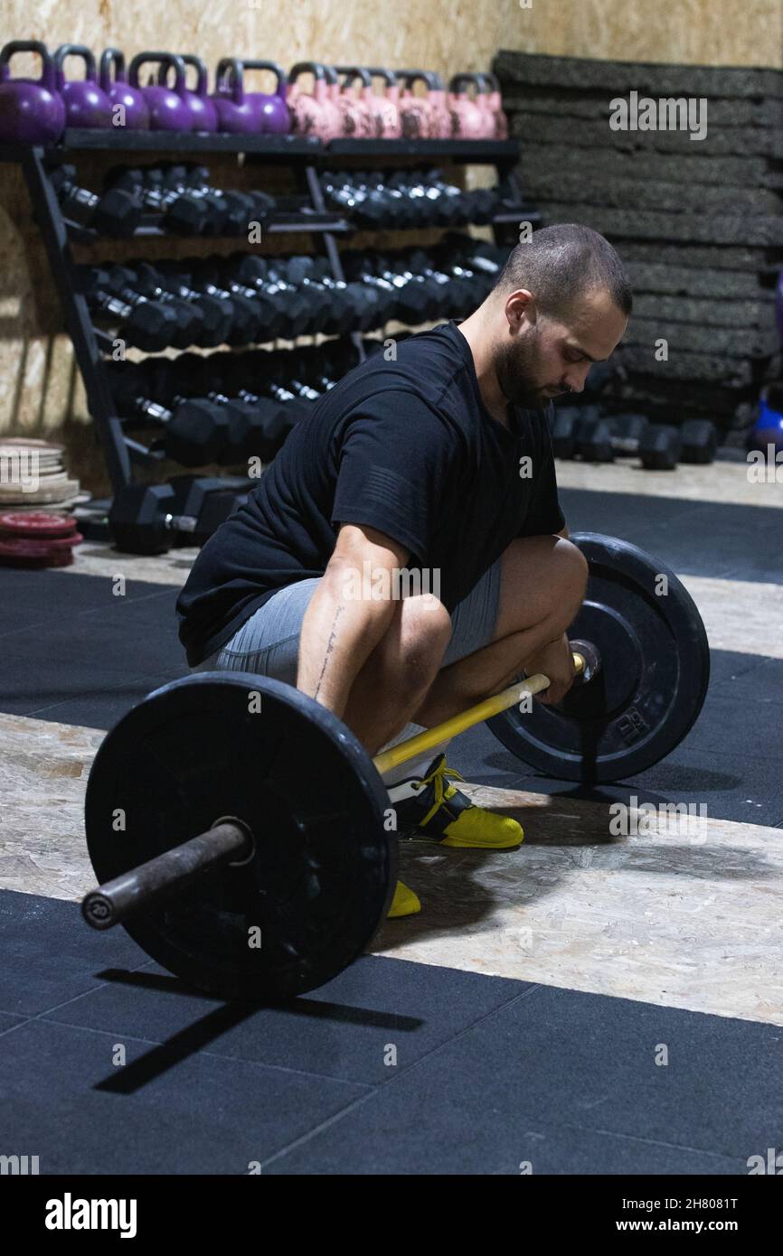 Corps complet d'athlète hispanique barbu focalisé de sexe masculin s'accroupir avec une barbell lourde pour faire de l'exercice de levée d'haltères pendant l'entraînement d'haltérophilie dans le centre sportif Banque D'Images