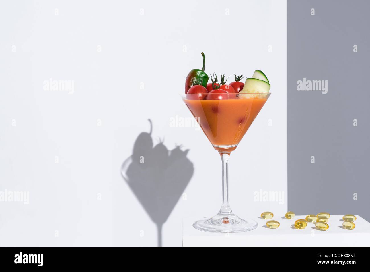 Soupe fraîche de gazpacho avec tomates cerises et concombres servis dans un verre à cocktail placé sur un support blanc sur fond gris Banque D'Images