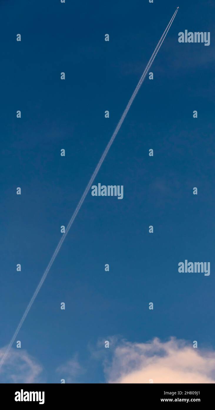 Un avion traverse le ciel bleu en diagonale, laissant derrière eux une longue piste blanche Banque D'Images