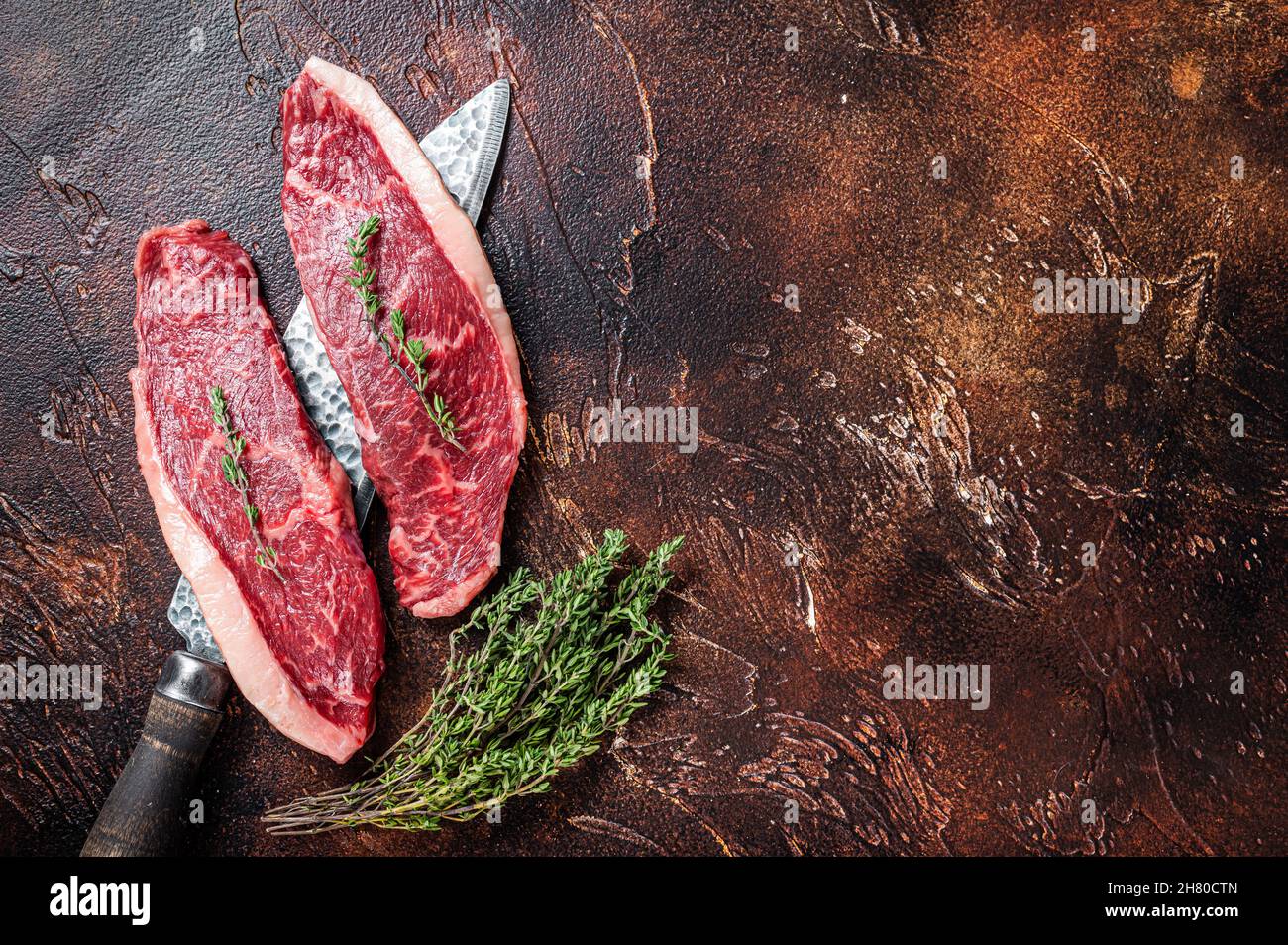 Chapeau de sirloin cru non cuit ou steaks de viande de bœuf sur un couteau de boucher. Arrière-plan sombre. Vue de dessus. Copier l'espace Banque D'Images