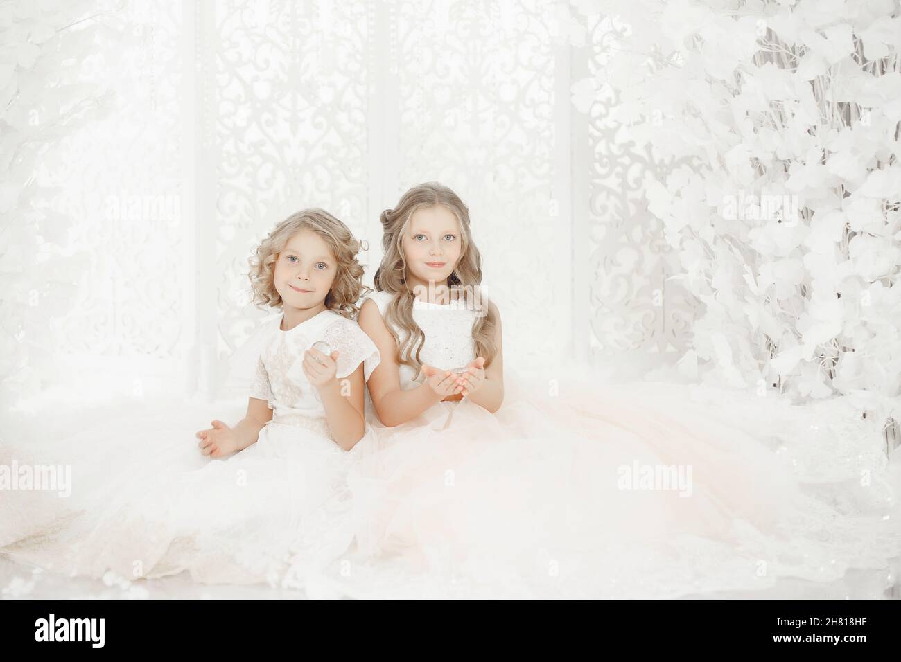 Jeune petite fille modèle blanc communion robe d'hiver se tient en couronne d'or avec des gemmes chères sous la neige lourde en studio sur fond gris Banque D'Images