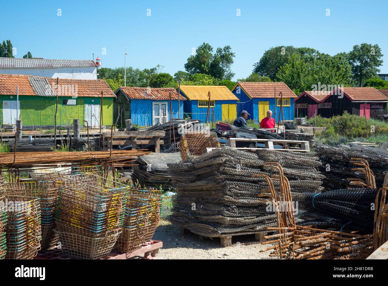 Île d'Oléron, Charente-Maritime, France - 7 juin 2014 : deux pêcheurs expérimentés conversant devant des huttes d'huîtres colorées dans le port du village Banque D'Images