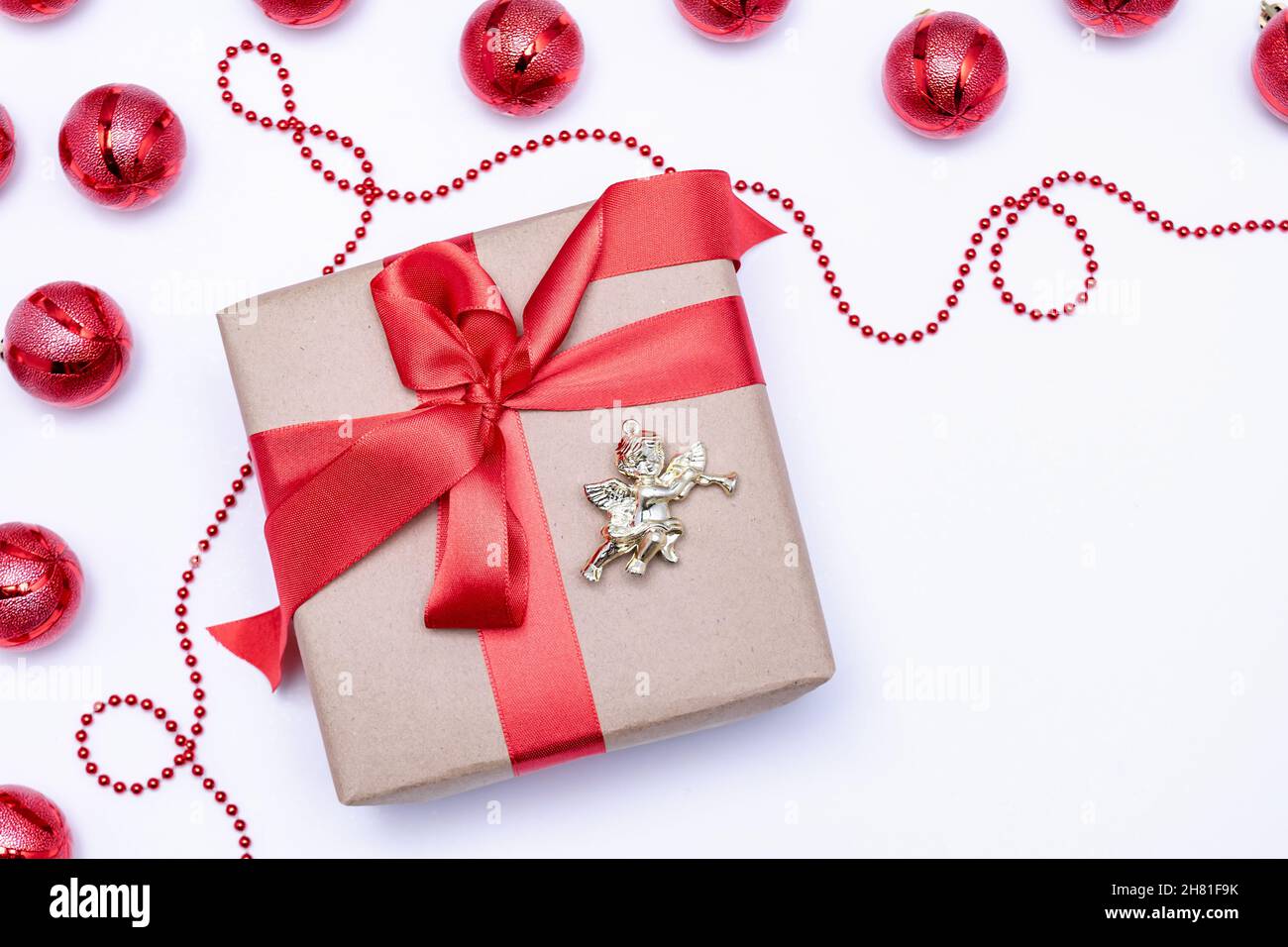 Sur fond blanc, un cadeau avec un ruban rouge et un ange à côté des boules de Noël rouges.Carte postale de fête.Photo horizontale. Banque D'Images Sur fond blanc, un cadeau avec un ruban rouge et un ange à côté des boules de Noël rouges.Carte postale de fête.Photo horizontale. Banque D'Images