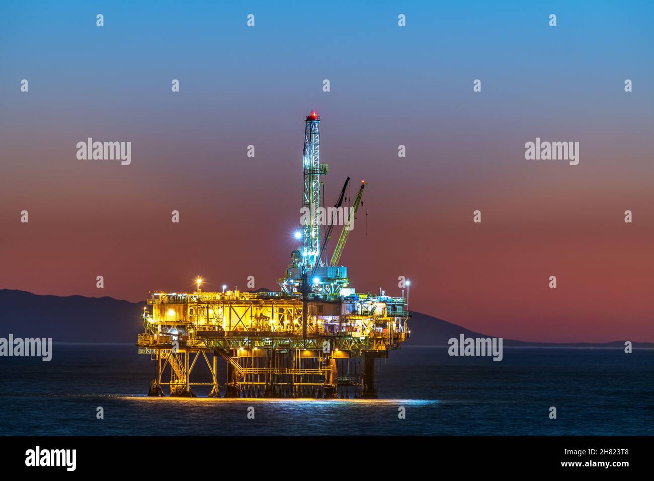 Plate-forme pétrolière offshore au large des côtes de la Californie contre un ciel orange et sombre alors que le soleil se couche derrière la plate-forme. Banque D'Images