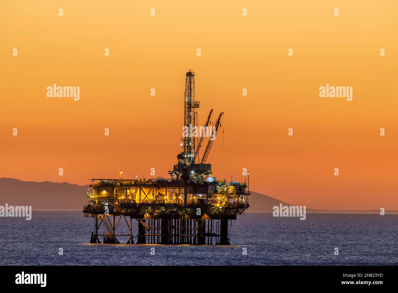 La plate-forme pétrolière offshore au large de la côte californienne se fixe contre un ciel orange rempli de fumée d'un feu à proximité tandis que le soleil se couche derrière la plate-forme. Banque D'Images