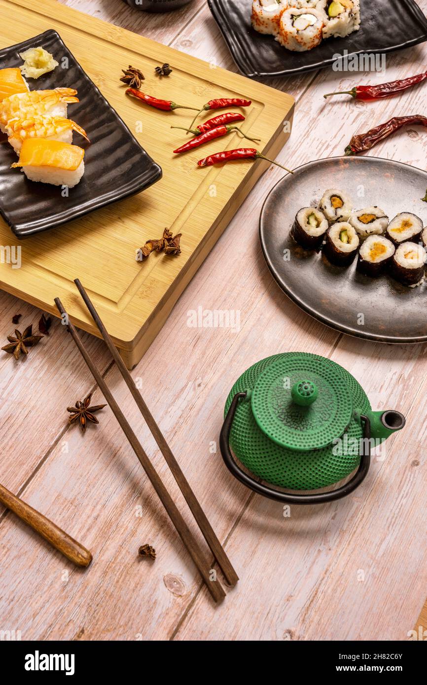 Encore la vie avec un pot de thé vert en fonte, des baguettes en bois et des sushis maki au saumon, nigiri, piments rouges chauds, anis étoilé et planche en bambou Banque D'Images