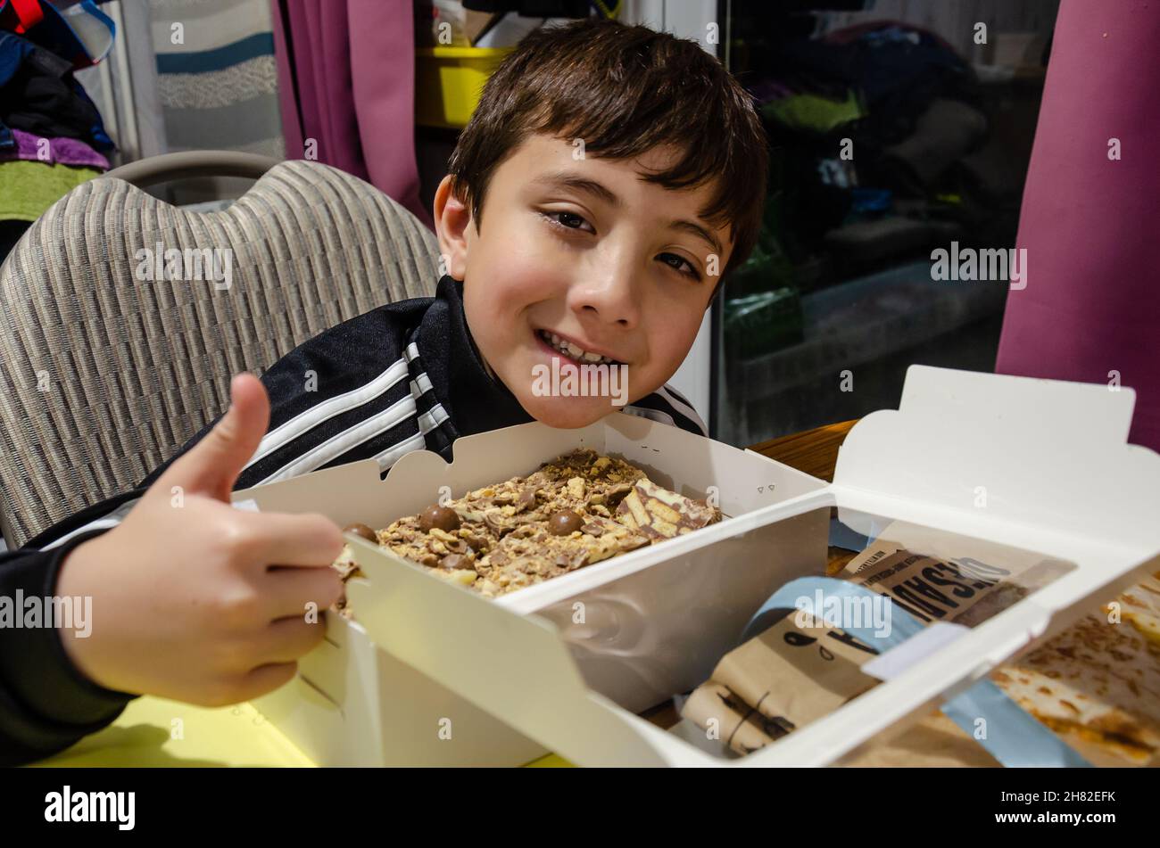 Un garçon donne son approbation de pouce un sourire à la caméra en réponse à l'ouverture d'une boîte de tiffin. Banque D'Images