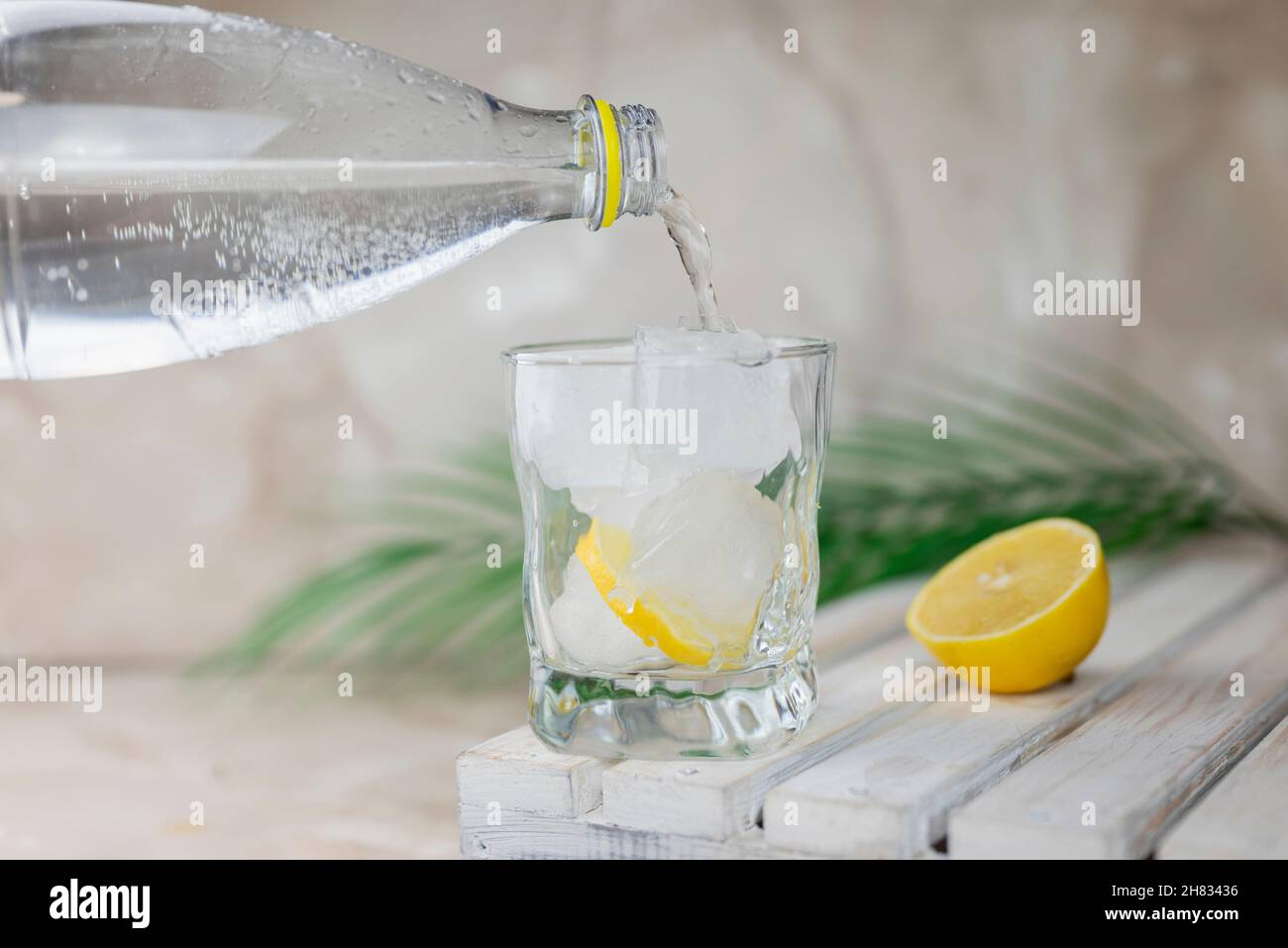 de l'eau ou du tonique est versé d'une bouteille dans un verre avec de la glace et du citron Banque D'Images