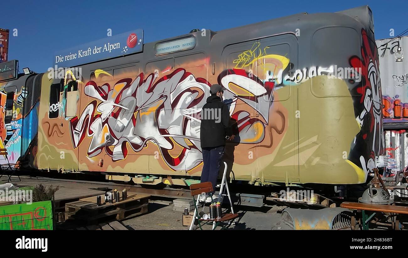 Artiste pulvérisant des graffitis sur une voiture abandonnée dans la zone du projet culturel de Bahnwaerter Thiel, Munich, Bavière, Allemagne. Banque D'Images