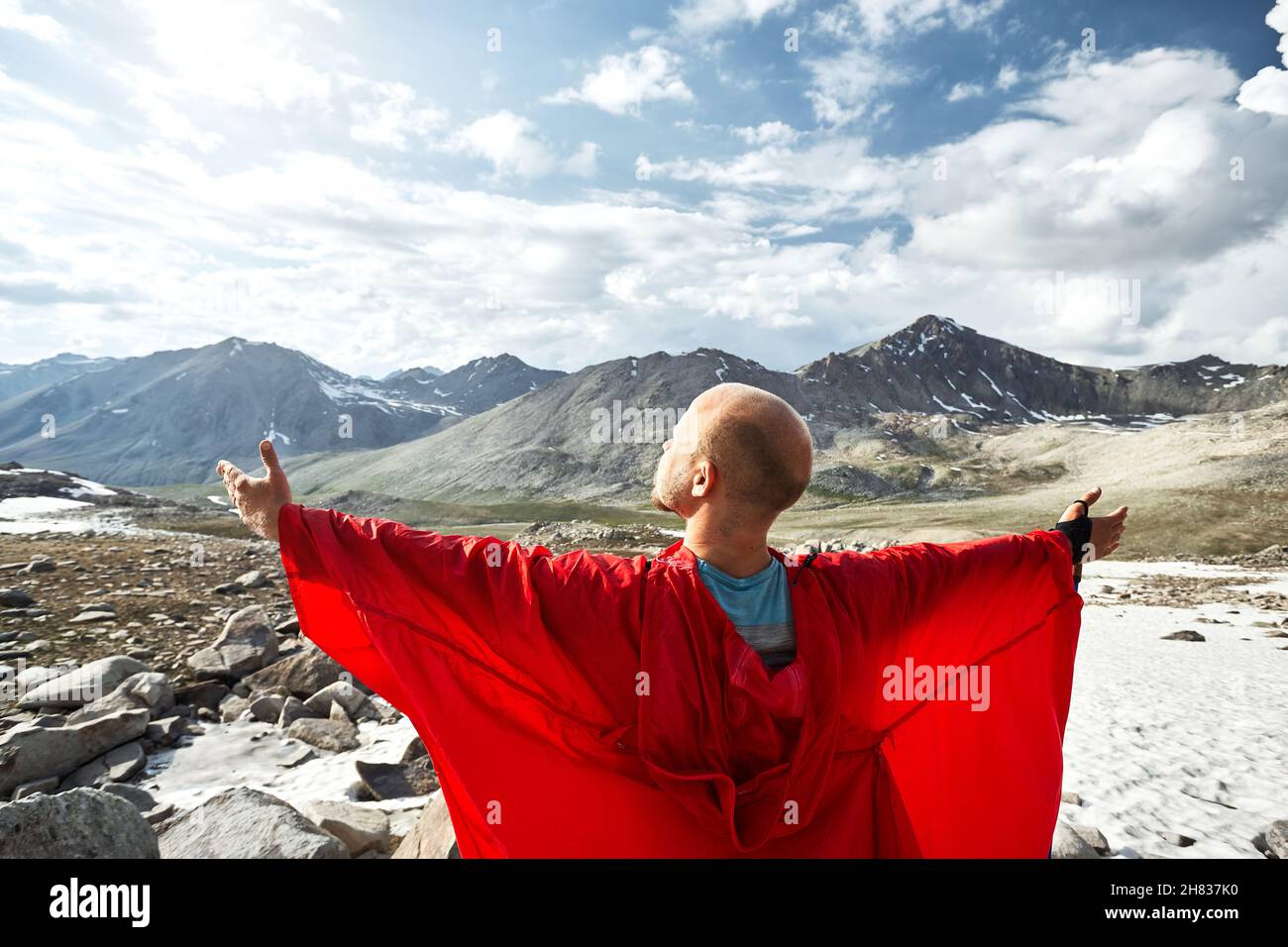 Homme en couverture de pluie rouge sur le rocher large a étendu ses mains dans les belles montagnes contre le ciel bleu Banque D'Images