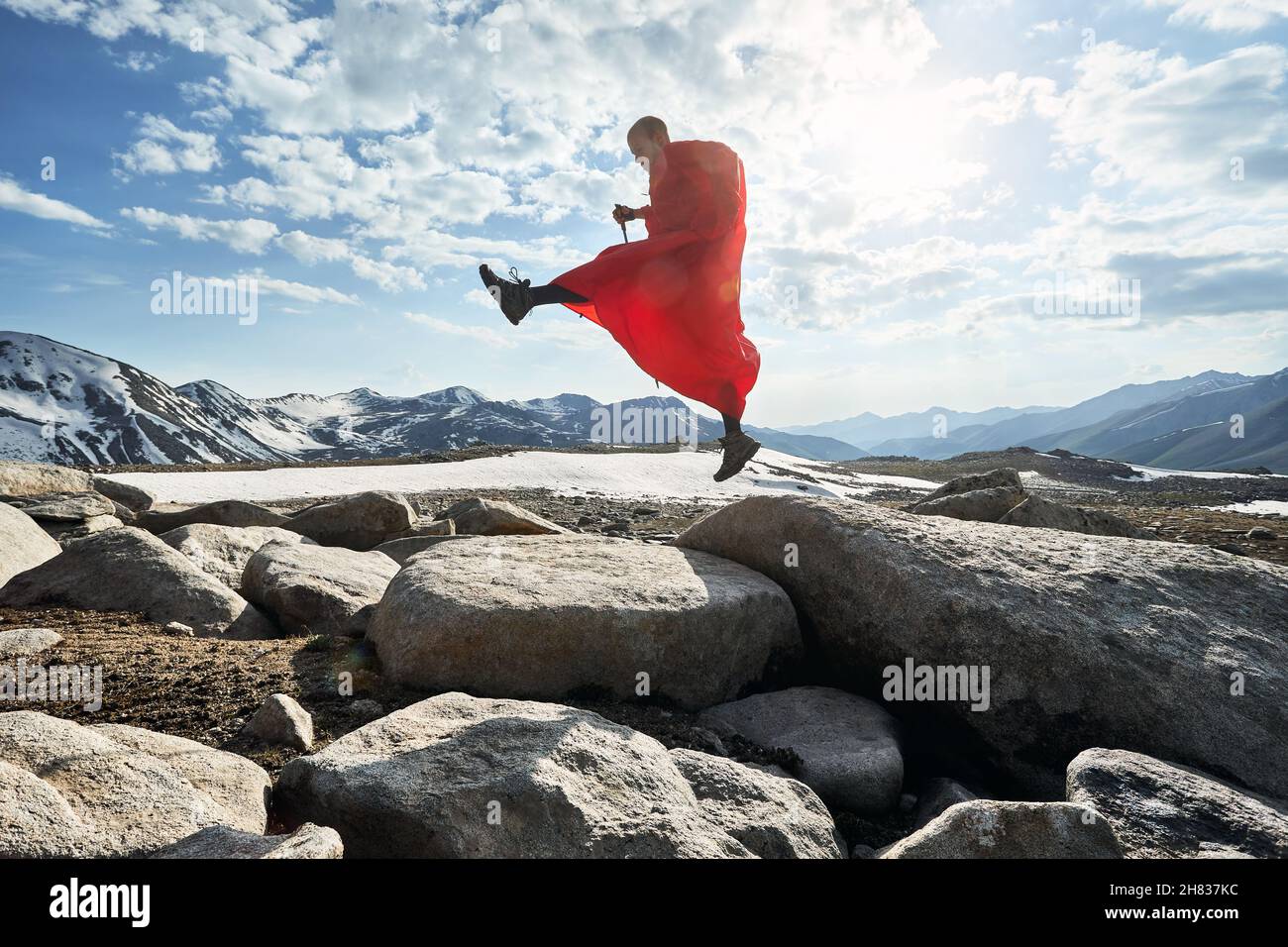 Homme en couverture de pluie rouge sur le rocher dans les belles montagnes contre le ciel bleu Banque D'Images