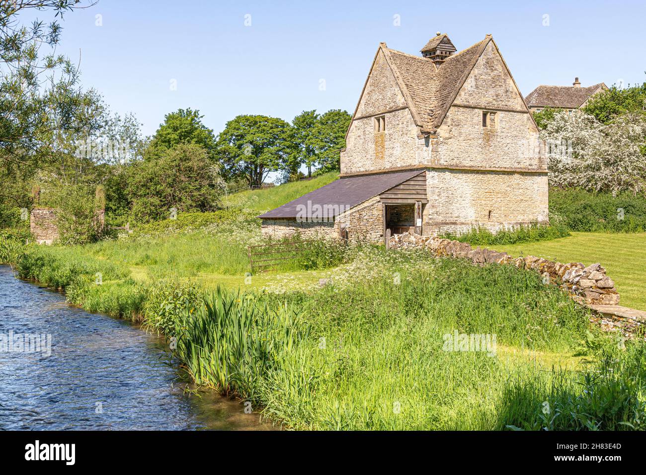 Le vieux pigeonnier de pierre (c. BJIJAD) à côté de la rivière Windrun naissante, qui coule à travers le village de Cotswold de Naunton, Gloucestershire, Royaume-Uni Banque D'Images