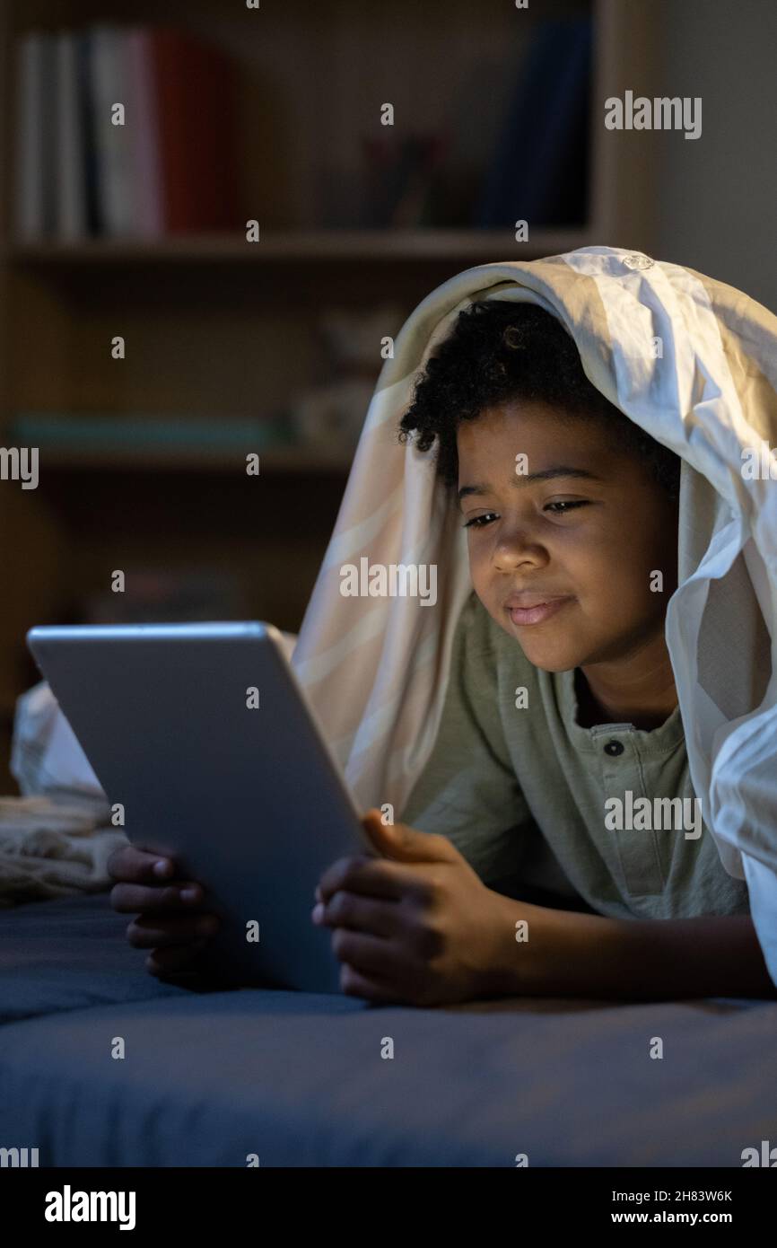 Contenu Afro-américain garçon couché avec une tablette sous couette dans la chambre noire de bébé Banque D'Images