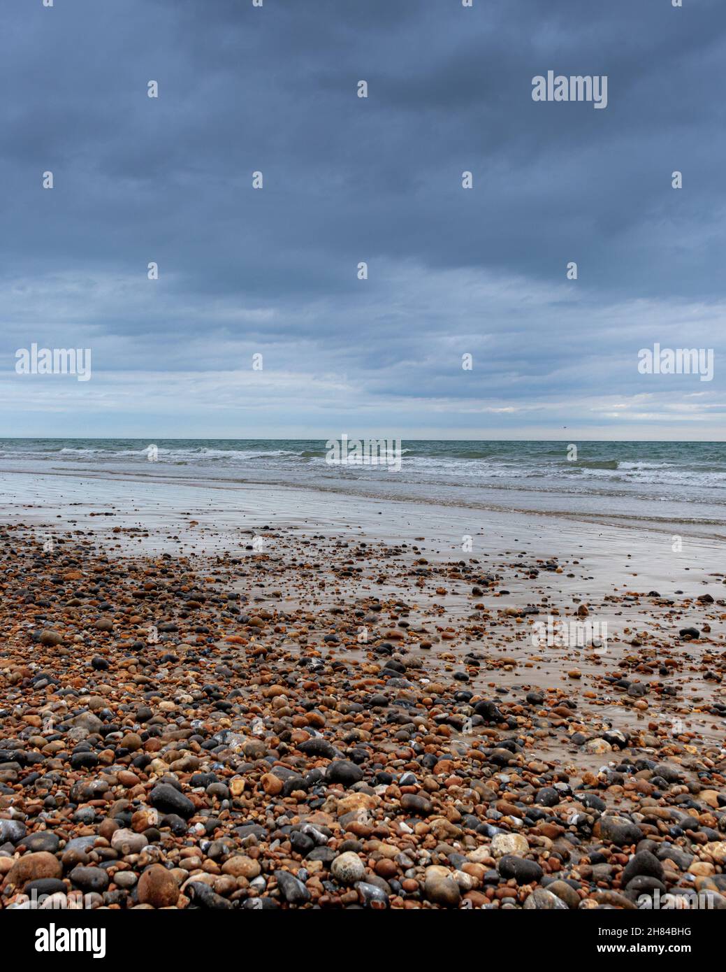 Pebble Beach avec sable, set et de petites vagues sous le ciel de moody à Hastings dans Sussex, Angleterre. Banque D'Images